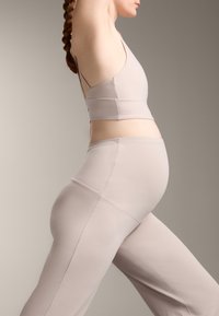 Komplet aktivne obleke za nosečnice iz mehkega, svetlega bež blaga. Vključuje prilegajoč se top s tankimi naramnicami in legice visoke pasu z okvirnimi detajli.