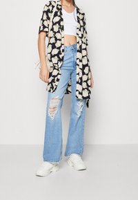 Černý kimono s květinovým vzorem přes bílé crop top, sladěné s světle modrými roztrhanými širokými džíny a bílými teniskami.