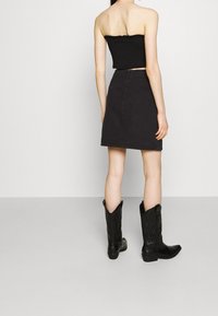 Svart strapless topp kombinerad med en högmidjad svart denimkjol och knähöga svarta cowboyboots med intrikata mönster.