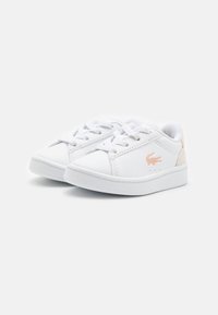 Hvite joggesko laget av syntetisk materiale, med en glatt overflate, snøring og en subtil preget logo i lys oransje.