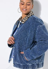 Pikowana kurtka dżinsowa w kolorze niebieskim z kołnierzem z futra w panterkę, srebrnym wykończeniem i bocznymi kieszeniami. Charakteryzuje się luźnym krojem i teksturowaną tkaniną.
