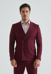 Veste de costume bordeaux croisée avec deux poches avant, accents de boutons et une chemise légère à motifs floraux en dessous. Ajustement sur mesure.