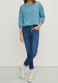 Sweatshirt bleu clair à col rond et manches à volants, associé à un jean bleu foncé et des baskets montantes blanches.