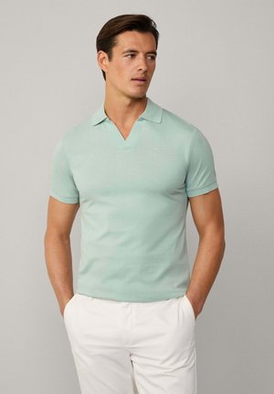 Polo de manga corta azul claro, hecho de algodón suave, con un escote en V y un pequeño detalle del logo en el lado izquierdo del pecho. Combinado con pantalones blancos.