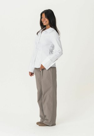 White button-up shirt with long sleeves and wide cuffs paired with loose, light brown trousers. Smooth fabric texture, no visible patterns.