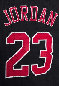 Schwarzes Basketballtrikot mit dem Namen "JORDAN" in rot und der Nummer "23" in einer kräftigen roten Schrift, weiß umrandet. Hergestellt aus Mesh-Material.