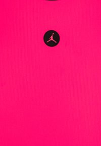 T-shirt en tissu côtelé rose vif présentant un logo noir rond avec une silhouette rose d'une figure dans une pose de saut au centre.
