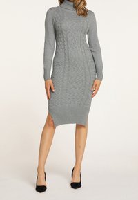 Robe en tricot grise avec col roulé, poignets côtelés et fentes sur les côtés. Motif texturé courant verticalement le long du corps.