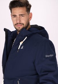 Giacca a hood blu navy con finitura liscia e opaca, dotata di lacci bianchi, logo sopra il petto e tasche con cerniera.