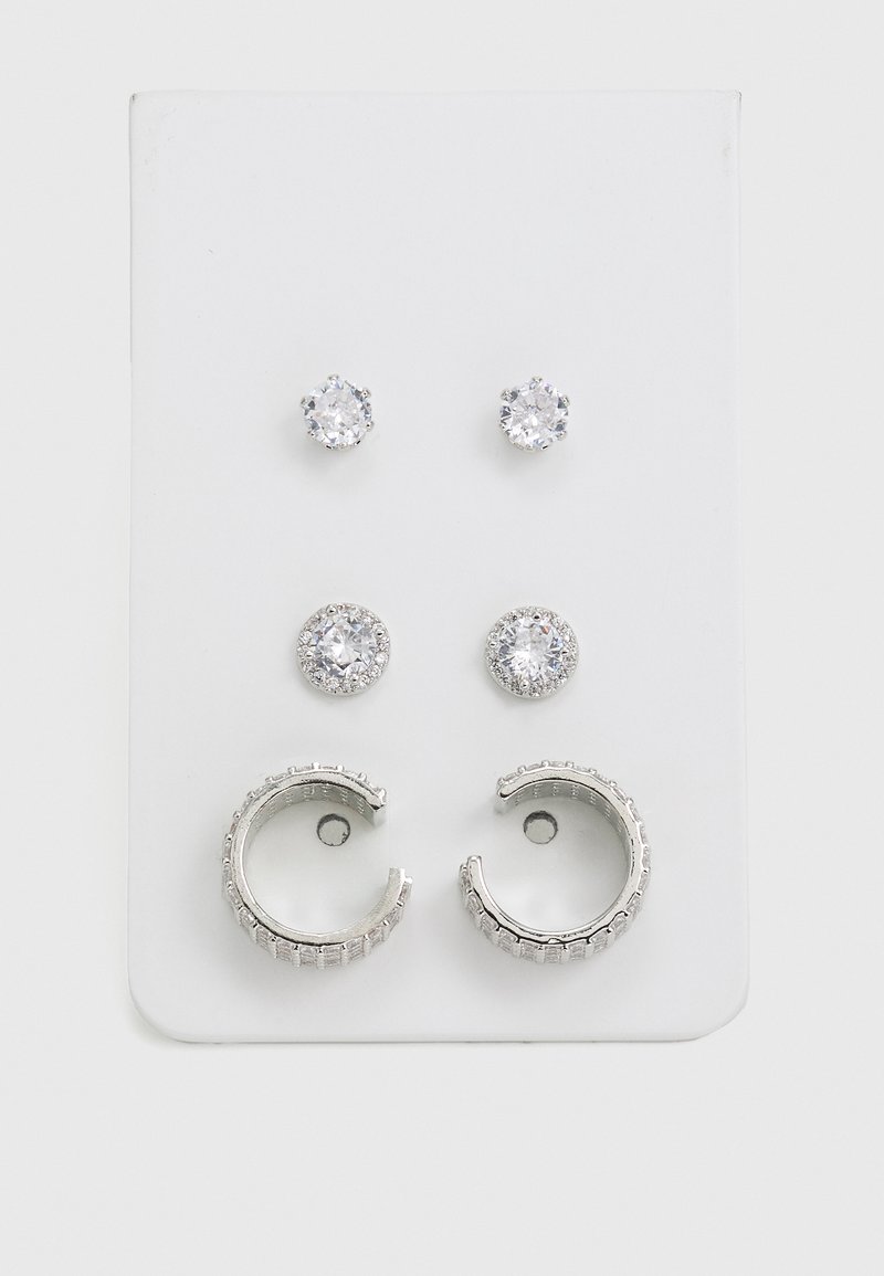Juego de tres pares de aretes: dos pares de aretes de botón con piedras redondas y transparentes, y un par de aros de plata con bandas texturizadas.