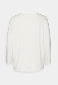 Vit långärmad skjorta i mjukt material med avslappnad passform, bred hals och sänkta axlar. Enkel design utan synliga mönster.