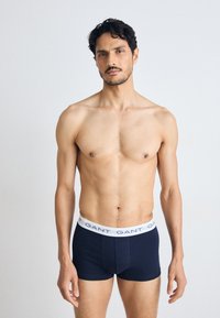 Marineblå herreboxershorts med en hvid elastisk talje, der har brandtekst. Glat bomuldsstof, tætsiddende form og kort benlængde.