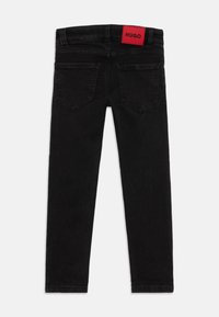 Jean en denim noir avec une coupe slim, design à cinq poches et une étiquette rouge "HUGO" sur la taille. Texture lisse avec des dégradés subtils.