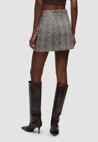 Sort-hvid houndstooth-mønstret miniskirt med en glat tekstur, kombineret med høje, blanke brune hæle støvler.
