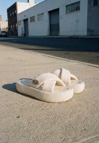 Paire de sandales à plateforme blanches tissées avec des brides croisées sur un trottoir en béton dans une zone urbaine avec des bâtiments en arrière-plan.