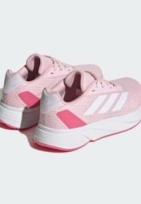 Scarpe sportive rosa con una tomaia in tessuto testurizzato, logo a tre strisce bianche, dettagli bianchi sul tallone e suola rosa a contrasto.