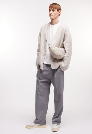 Cárdigan de punto gris claro, camiseta blanca, pantalones grises holgados y zapatillas blancas. El modelo lleva un bolso bandolera acolchado en color beige.