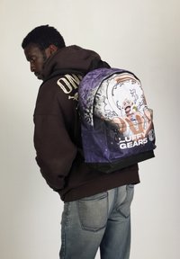 La mochila presenta un diseño en púrpura y negro, con un personaje ilustrado en el frente y una tela duradera. Incluye un bolsillo frontal y correas ajustables.