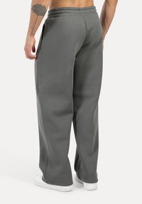 Pantalones de chándal grises con un corte relajado, fabricados en material suave, con una cintura elástica y bolsillos laterales. Combinados con zapatillas blancas.