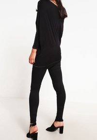 Maglietta nera oversize con maniche lunghe, caratterizzata da cuciture in contrasto. Indossata con leggings neri aderenti e tacchi neri aperti.