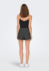 Zwarte cami gecombineerd met donkergrijze, op maat gemaakte shorts. De shorts hebben een gladde textuur en twee achterzakken. Witte sneakers maken de look af.
