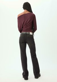 Dugi rukav maroon majica s off-shoulder dizajnom, uparena s crnim trapericama visokog struka koje imaju srebrni detalj na remenu i boot-cut nogavicama.