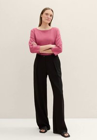 Vaaleanpunainen, kolmivartinen paita yhdistettynä löysiin mustiin housuihin. Asu on yksinkertainen, suora leikkaus ja vähäiset yksityiskohdat.