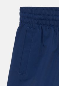 Navy blue shorts featuring an elastic waistband, smooth texture, and accent stitching. Includes a side pocket on the left.