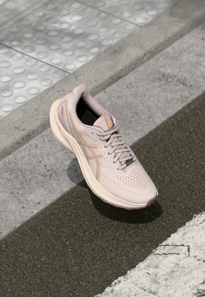 Chaussure de sport rose clair avec tige en mesh, lacets et semelle en caoutchouc ; présente des accents orange subtils et un motif texturé sur le bout.