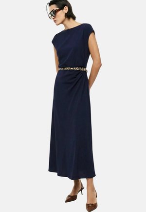 Donna che indossa un vestito midi smanicato blu navy con cintura leopardata, tacchi marroni a punta e grandi occhiali da sole neri.