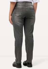Pantalones de mezclilla grises con cintura ajustada, piernas rectas, cinco bolsillos y sutiles detalles de costura. Combinados con zapatos negros.