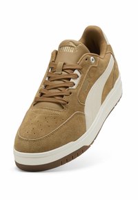 Baskets en daim marron avec accents en cuir blanc, bout arrondi, tige perforée et lacets plats. Elles possèdent une semelle en caoutchouc et un logo Puma sur la languette.