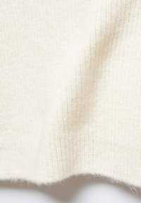 Teksturowana, żebrowana tkanina w kolorze kremowym, miękka i puszysta. Materiał wykazuje subtelne różnice w grubości i gęstości, z lekko puszystym brzegiem.