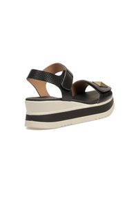 Sandal de plataforma de cuero negro con correas anchas y un acento metálico cuadrado, con una superficie texturizada y una suela de goma crema en contraste.