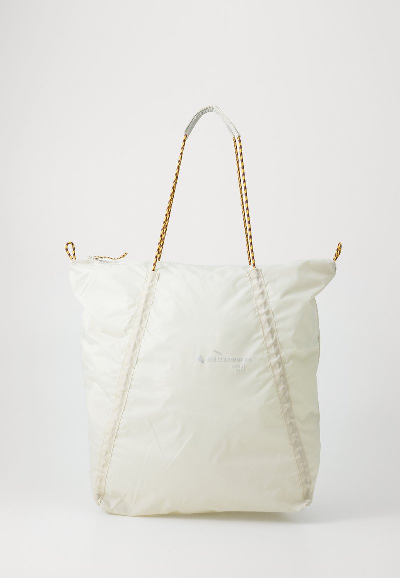 Stor hvit totebag laget av skinnende materiale, med flettede gullstropper og et sydd design. Glidelås lukking på toppen.