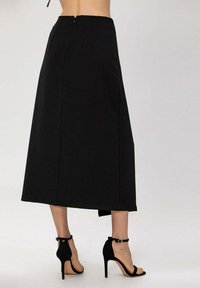 Jupe maxi noire à coupe droite, dotée d'une fermeture éclair au dos et de détails de couture subtils, complétée par des chaussures à talons hauts noires à lanières.