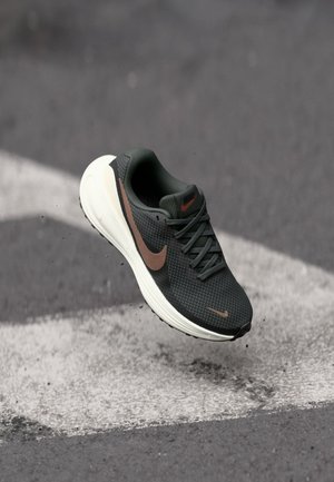 Black mesh running shoe with a textured upper, a brown Nike swoosh, and a white cushioned sole, suspended above a gray surface.