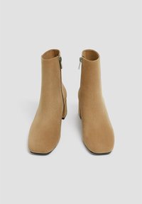 Bottes ankle en suède tan avec un bout carré et un talon bloc de hauteur intermédiaire. Présente une fermeture éclair sur le côté et une texture lisse.