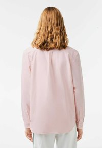 Camicia a maniche lunghe rosa chiaro realizzata in tessuto morbido, con polsini con bottone, vestibilità rilassata e dettaglio sulla spalla posteriore.