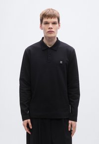 Μαύ ρο πόλο μπλουζάκι με μακριά μανίκια, γιακά και λωρίδα με κουμπιά. Διαθέτει μικρό λογότυπο στο στήθος και άνετη εφαρμογή. Ομαλή, απαλή υφή.