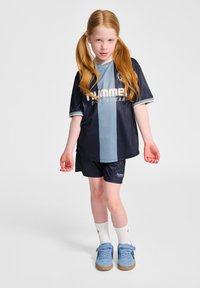 Marinblå och ljusblå sporttröja med horisontella ränder och vit logotyp, kombinerad med marinblå shorts. Modellen bär blå skor och vita strumpor.