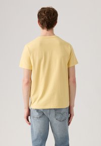 Camiseta amarilla de manga corta hecha de algodón, con un diseño sencillo y un dobladillo recto, combinada con jeans de mezclilla azul claro.