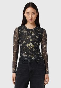 Μαύρο μπλουζάκι με μακριά μανίκια και λουλουδάτο μοτίβο σε κίτρινο και λευκό, κατασκευασμένο από διαφανές υλικό, με στρογγυλή λαιμόκοψη και στενή γραμμή.