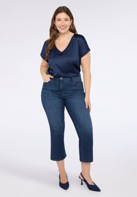 Navy satiininen V-kaula-aukkoinen paita yhdistettynä tummansinisiin farkkuleikkauksiin ja tummansinisiin korkokenkiin, joissa on hienovaraisia ompeleita ja koristeelliset taskut.