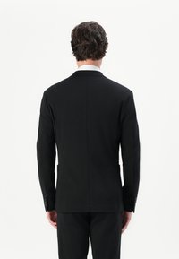Schwarze maßgeschneiderte Anzugjacke mit Reverskragen, einzelnem Schlitz und geknöpften Bündchen. Glatter Stoff mit matter Oberfläche und strukturiertem Silhouette.