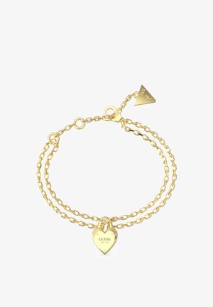 Bracelet double chaîne en or avec un charme en forme de cadenas en cœur portant l'inscription "GUESS EST. 1981" et une étiquette triangulaire.