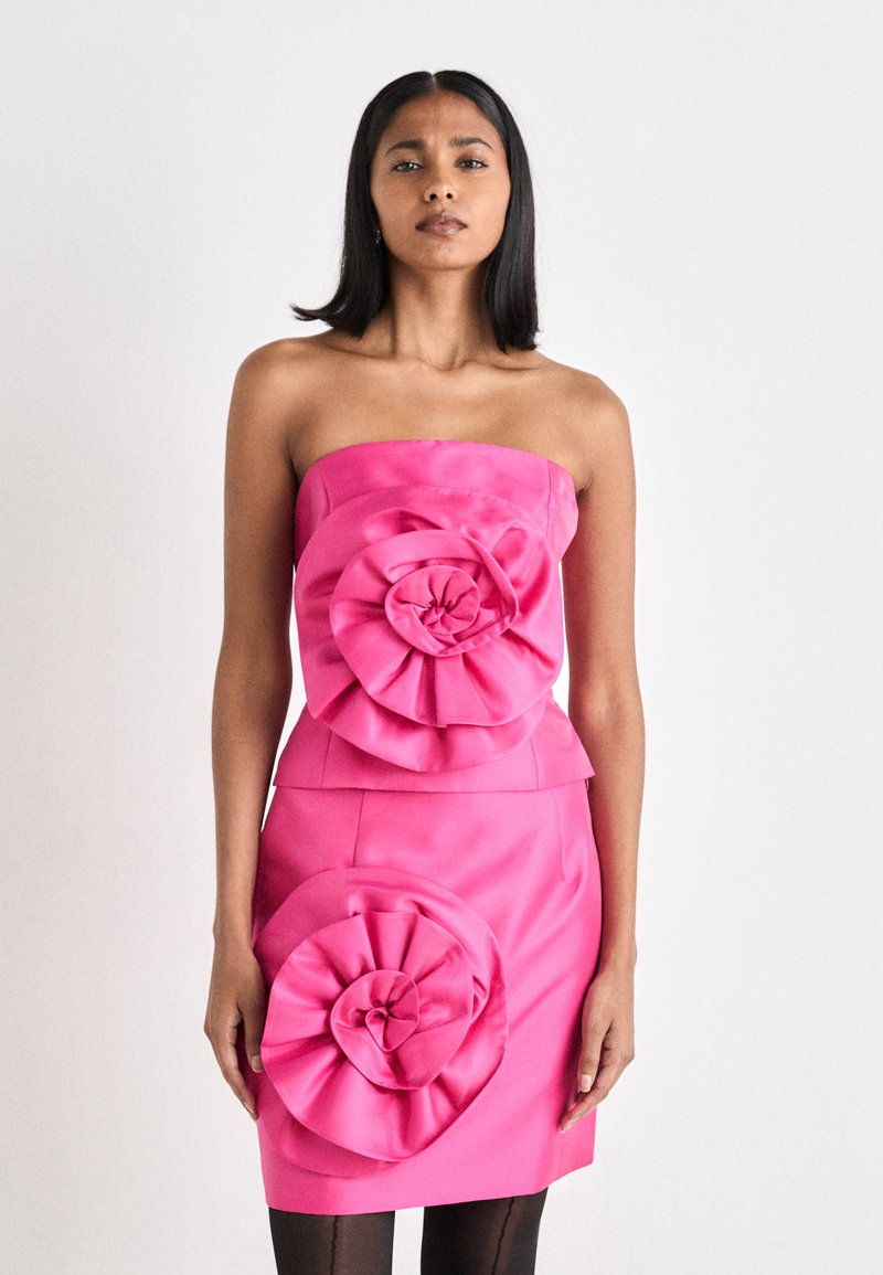 Uten skulderstropper rosa kjole med store, lagdelte blomsterdekorasjoner på bodice og skjørt. Glatt satengstoff, tettsittende silhuett.