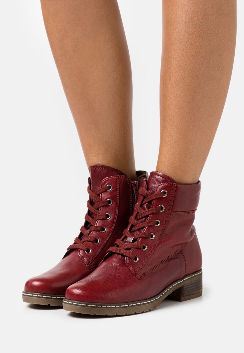 Botas de tobillo de cuero rojo con diseño de cordones, punta redonda y un tacón bajo apilado. Presentan ojales de metal y suela de goma cosida.