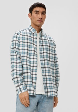 Geruite overhemd in wit, blauw en zwart; lichtgewicht stof, lange mouwen en één borstzak. Draagt over een wit T-shirt.