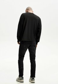 Cămașă neagră cu mâneci lungi și umeri căzuți, asociată cu blugi negri cu modele colorate de stropi. Încălțăminte: sneakers gri.